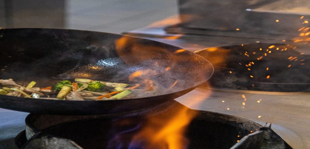 Vegetables searing in a wok over open flame at Textures